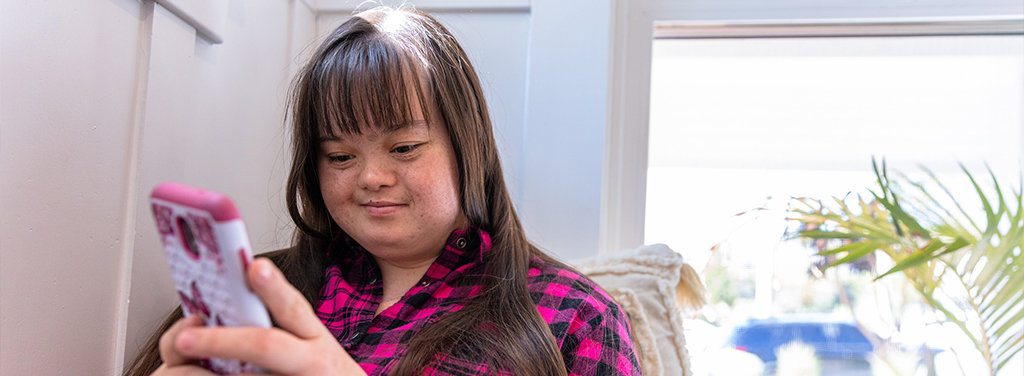 Young woman with Down's Syndrome using her smartphone by the window 